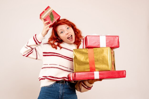 Vorderansicht der jungen Frau, die Weihnachtsgeschenke auf weißer Wand trägt