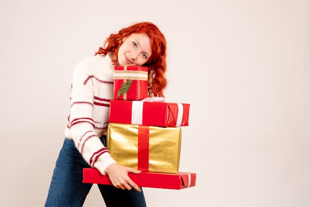 Vorderansicht der jungen Frau, die Weihnachtsgeschenke auf weißer Wand trägt