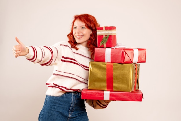 Vorderansicht der jungen Frau, die Weihnachtsgeschenke auf weißer Wand trägt