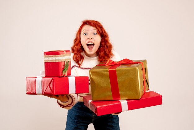 Vorderansicht der jungen Frau, die Weihnachtsgeschenke auf weißer Wand trägt