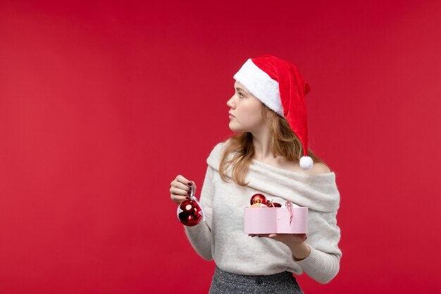 Vorderansicht der jungen Frau, die Weihnachtsspielzeug auf Rot hält