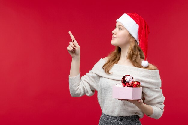 Vorderansicht der jungen Frau, die Weihnachtsspielzeug auf Rot hält