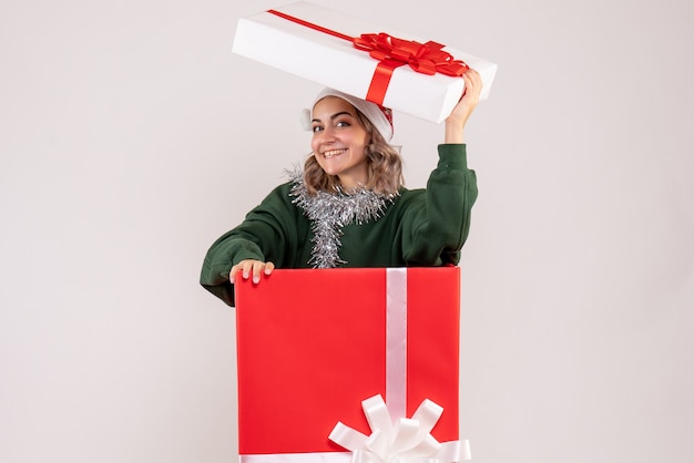 Vorderansicht der jungen Frau im roten Geschenkkarton lächelnd auf weißer Wand