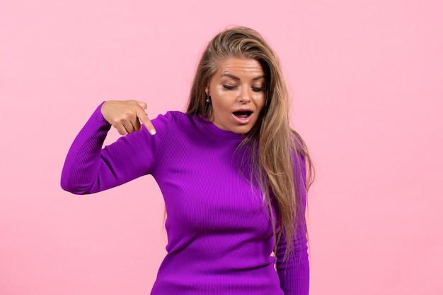 Vorderansicht der jungen Frau im schönen lila Kleid, die an der rosa Wand posiert