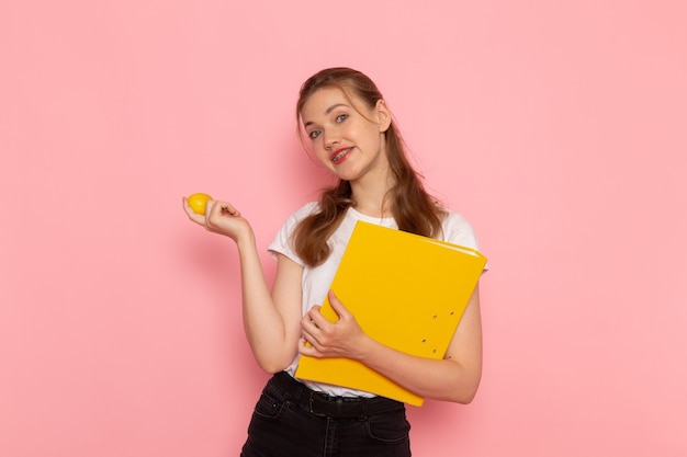Vorderansicht der jungen Frau im weißen T-Shirt, das frische Zitrone mit den auf der rosa Wand lächelnden Dateien hält
