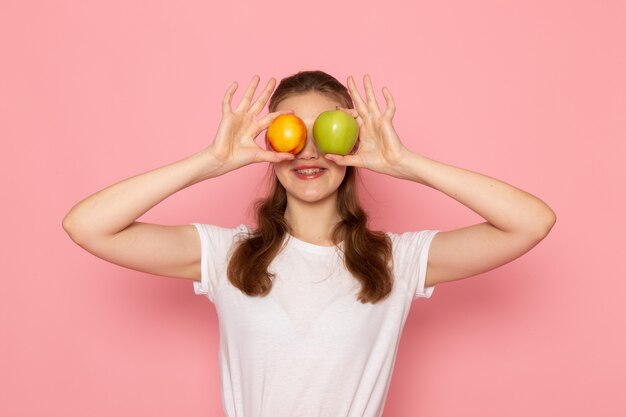 Vorderansicht der jungen Frau im weißen T-Shirt, das frischen grünen Apfel und Pfirsich hält
