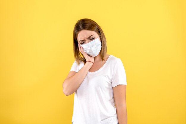 Vorderansicht der jungen Frau in der Maske auf einer gelben Wand