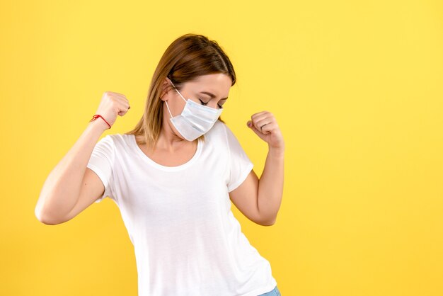 Vorderansicht der jungen Frau in der Maske auf einer gelben Wand