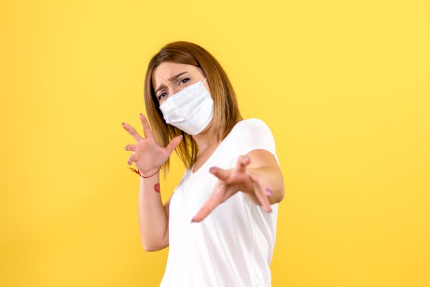 Vorderansicht der jungen Frau in der Maske auf einer gelben Wand