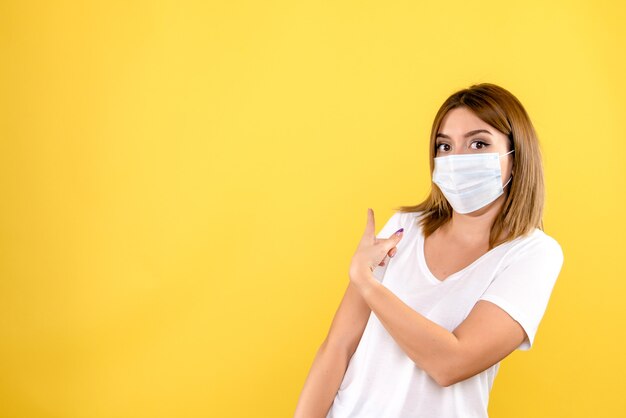 Vorderansicht der jungen Frau in der Maske auf einer gelben Wand