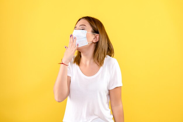 Vorderansicht der jungen Frau in der Maske auf einer gelben Wand