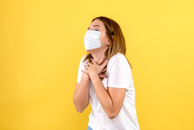 Vorderansicht der jungen Frau in der Maske auf einer gelben Wand