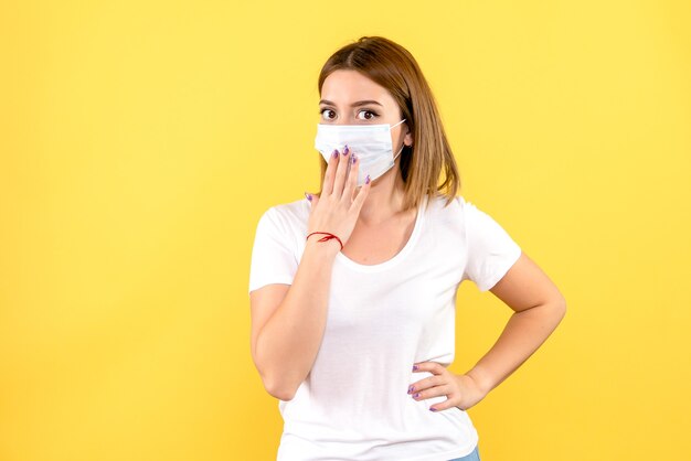 Vorderansicht der jungen Frau in der Maske auf einer gelben Wand