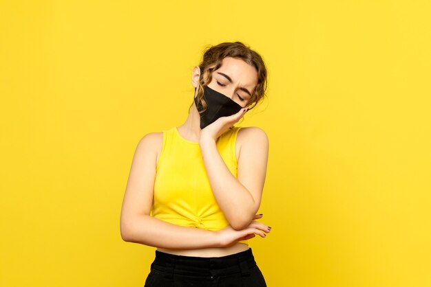 Vorderansicht der jungen Frau in der Maske auf gelber Wand