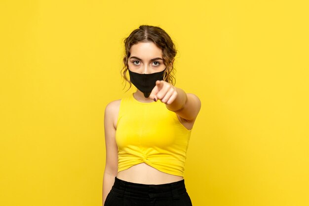 Vorderansicht der jungen Frau in der Maske, die auf gelbe Wand zeigt