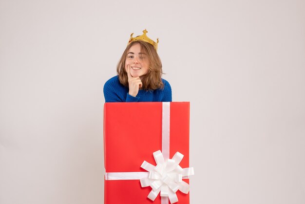 Vorderansicht der jungen Frau in der roten Geschenkbox an der weißen Wand