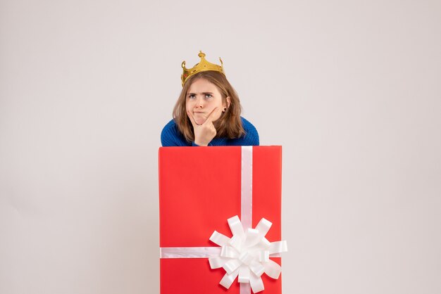 Vorderansicht der jungen Frau in der roten Geschenkbox an der weißen Wand