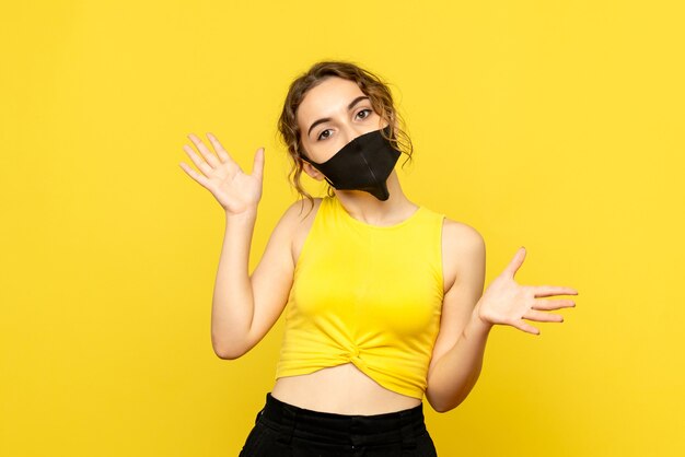 Vorderansicht der jungen Frau in der schwarzen Maske auf gelber Wand
