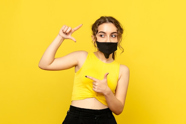 Vorderansicht der jungen Frau in der schwarzen Maske auf gelber Wand
