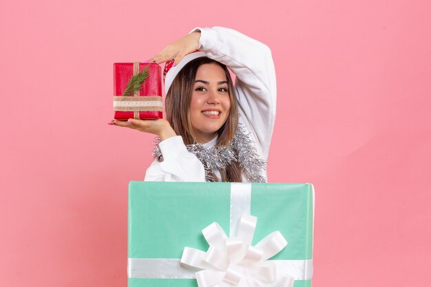 Vorderansicht der jungen Frau innerhalb des Geschenks, das ein anderes Geschenk auf einer rosa Wand hält