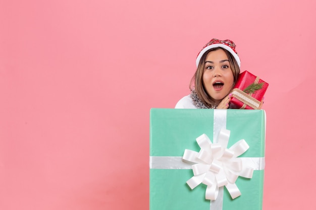 Vorderansicht der jungen Frau innerhalb des Geschenks, das ein anderes Geschenk auf einer rosa Wand hält