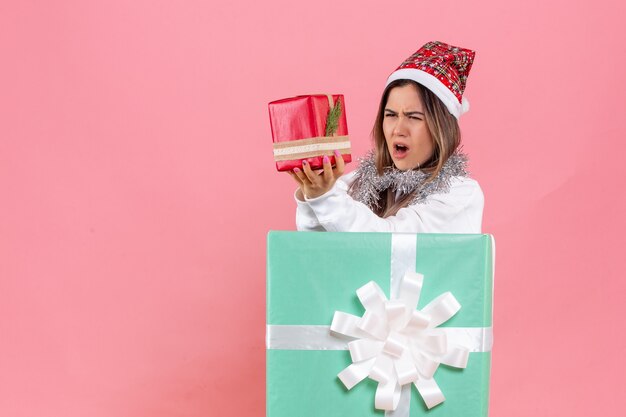 Vorderansicht der jungen Frau innerhalb des Geschenks, das ein anderes Geschenk auf einer rosa Wand hält