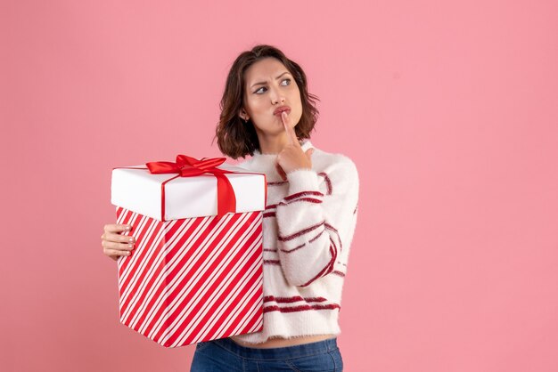 Vorderansicht der jungen Frau mit dem Weihnachtsgeschenk, das an rosa Wand denkt