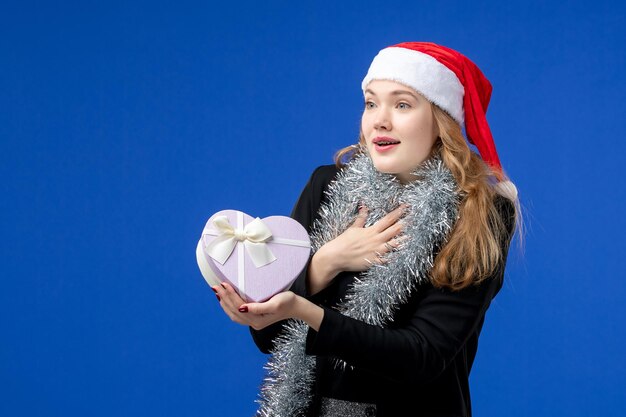 Vorderansicht der jungen Frau mit Feiertagsgeschenk an der blauen Wand