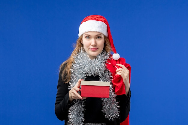 Vorderansicht der jungen Frau mit Feiertagsgeschenk an der blauen Wand