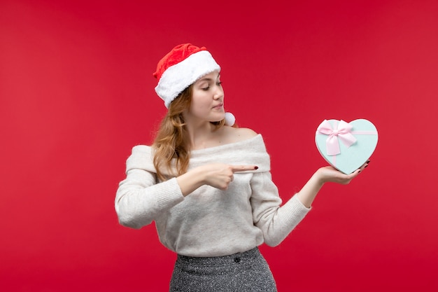 Vorderansicht der jungen Frau mit Geschenk auf rotem Boden Urlaub rotes Weihnachtsgeschenk