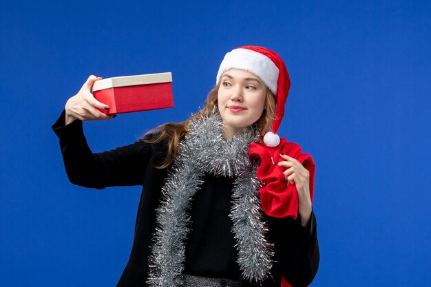 Kostenloses Foto vorderansicht der jungen frau mit geschenktüte und geschenk auf blauer wand