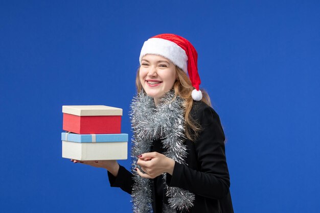 Vorderansicht der jungen Frau mit Neujahrsgeschenken an blauer Wand