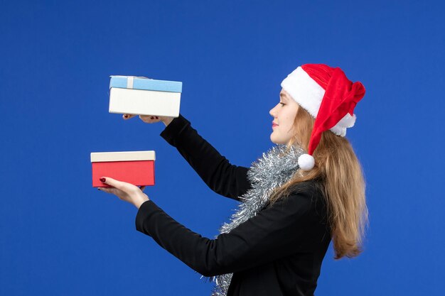 Vorderansicht der jungen Frau mit Neujahrsgeschenken an blauer Wand