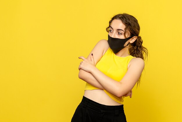 Vorderansicht der jungen Frau mit schwarzer Maske auf gelber Wand