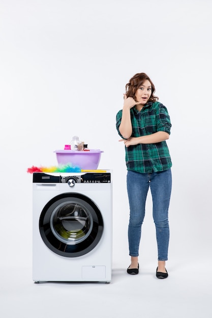 Vorderansicht der jungen Frau mit Waschmaschine an der weißen Wand