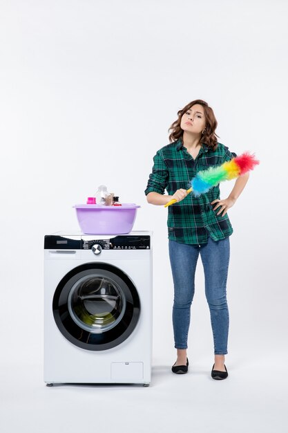Vorderansicht der jungen Frau mit Waschmaschine an der weißen Wand