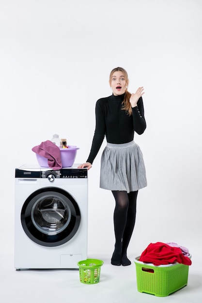 Vorderansicht der jungen Frau mit Waschmaschine und schmutziger Kleidung auf weißer Wand