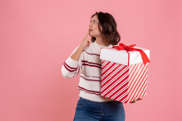 Vorderansicht der jungen Frau mit Weihnachtsgeschenk an der rosa Wand