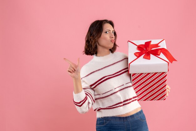 Vorderansicht der jungen Frau mit Weihnachtsgeschenk an der rosa Wand