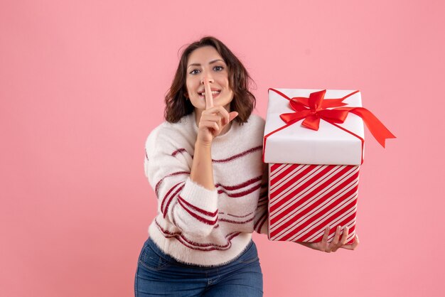 Vorderansicht der jungen Frau mit Weihnachtsgeschenk an der rosa Wand