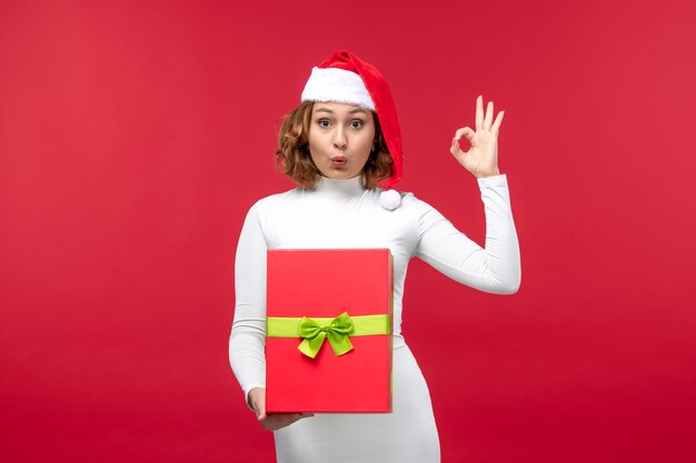 Vorderansicht der jungen Frau mit Weihnachtsgeschenk auf Rot
