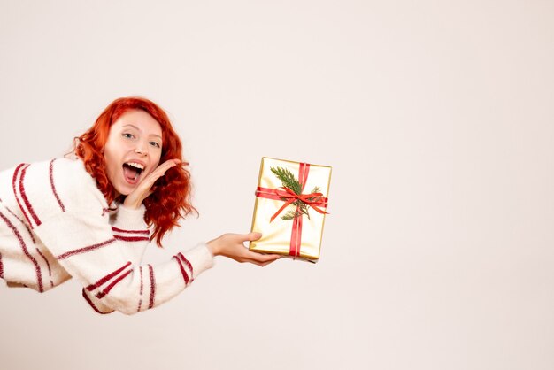 Vorderansicht der jungen Frau mit Weihnachtsgeschenk auf weißer Wand