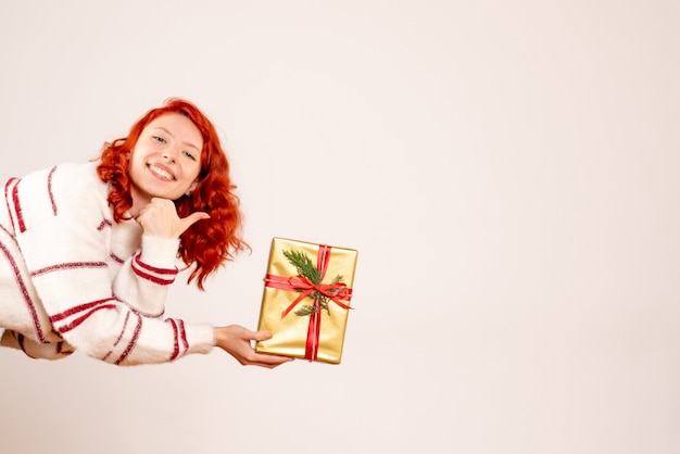 Vorderansicht der jungen Frau mit Weihnachtsgeschenk auf weißer Wand