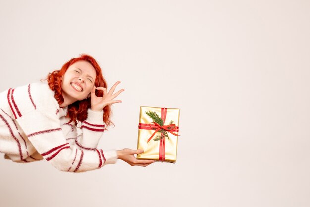 Vorderansicht der jungen Frau mit Weihnachtsgeschenk auf weißer Wand