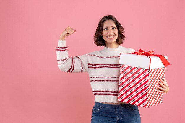 Vorderansicht der jungen Frau mit Weihnachtsgeschenk lächelnd auf rosa Wand