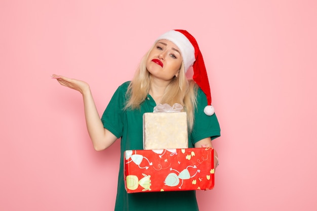 Vorderansicht der jungen Frau mit Weihnachtsgeschenken an der rosa Wand