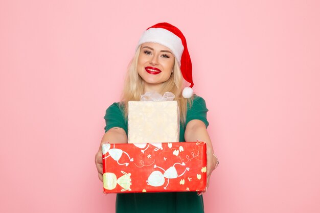 Vorderansicht der jungen Frau mit Weihnachtsgeschenken an der rosa Wand