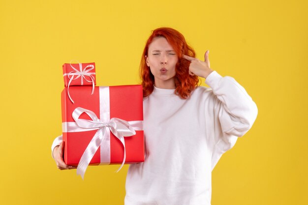 Vorderansicht der jungen Frau mit Weihnachtsgeschenken auf gelber Wand