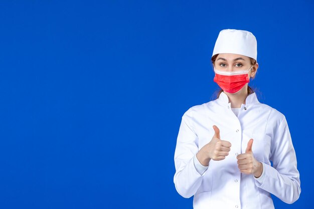 Vorderansicht der jungen Krankenschwester im medizinischen Anzug mit roter Maske auf Blau