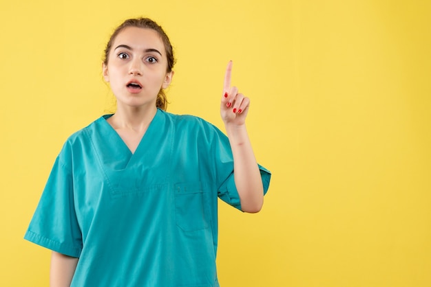 Vorderansicht der jungen Ärztin im medizinischen Anzug auf gelber Wand
